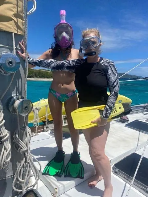 Two women in snorkeling gear holding fins on the boat