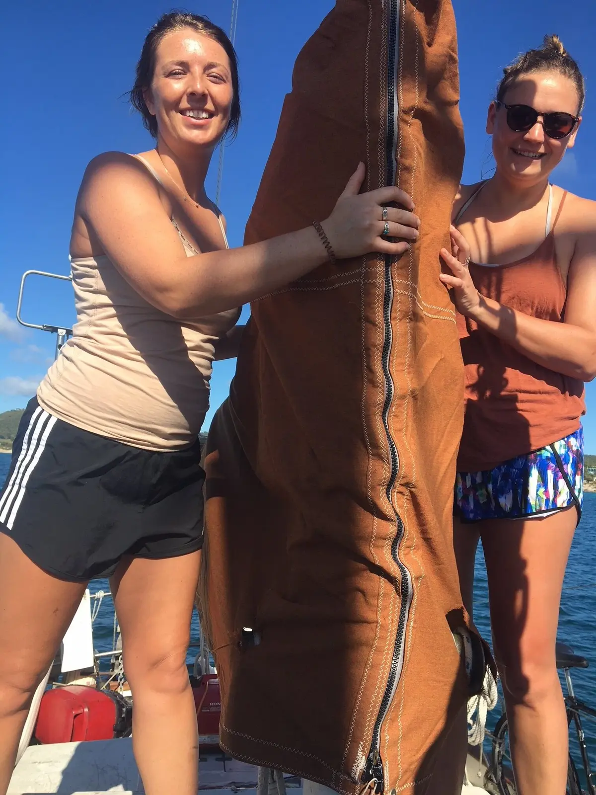 Two women smiling on the boat with a crew member between them under a bright blue sky