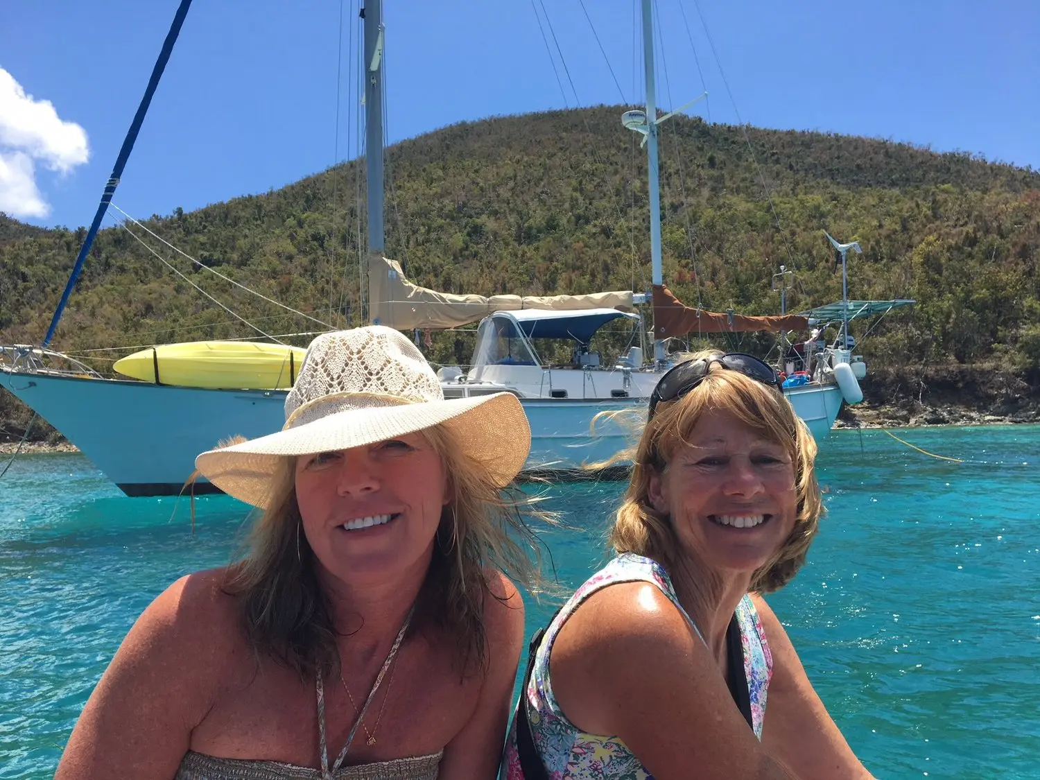 Two women enjoying a boat trip on turquoise water with green hills behind