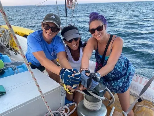 Guests helping haul in a line on the winch while sailing